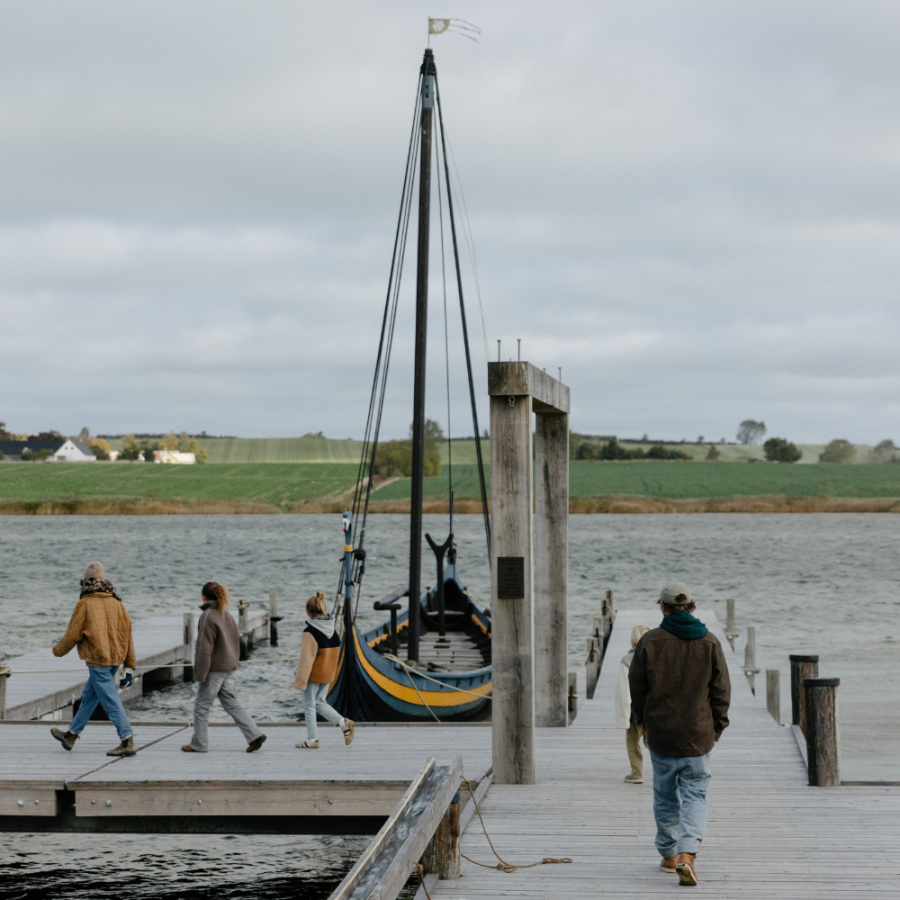 En familie er på vej ud på en flydende havn for at inspicere et replikeret vikingeskib en overskyet dag