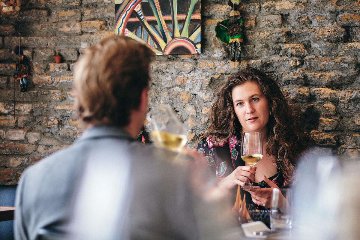 Kvinde og mand på restaurant med vinglas i hånden og rustikt murværk i baggrunden