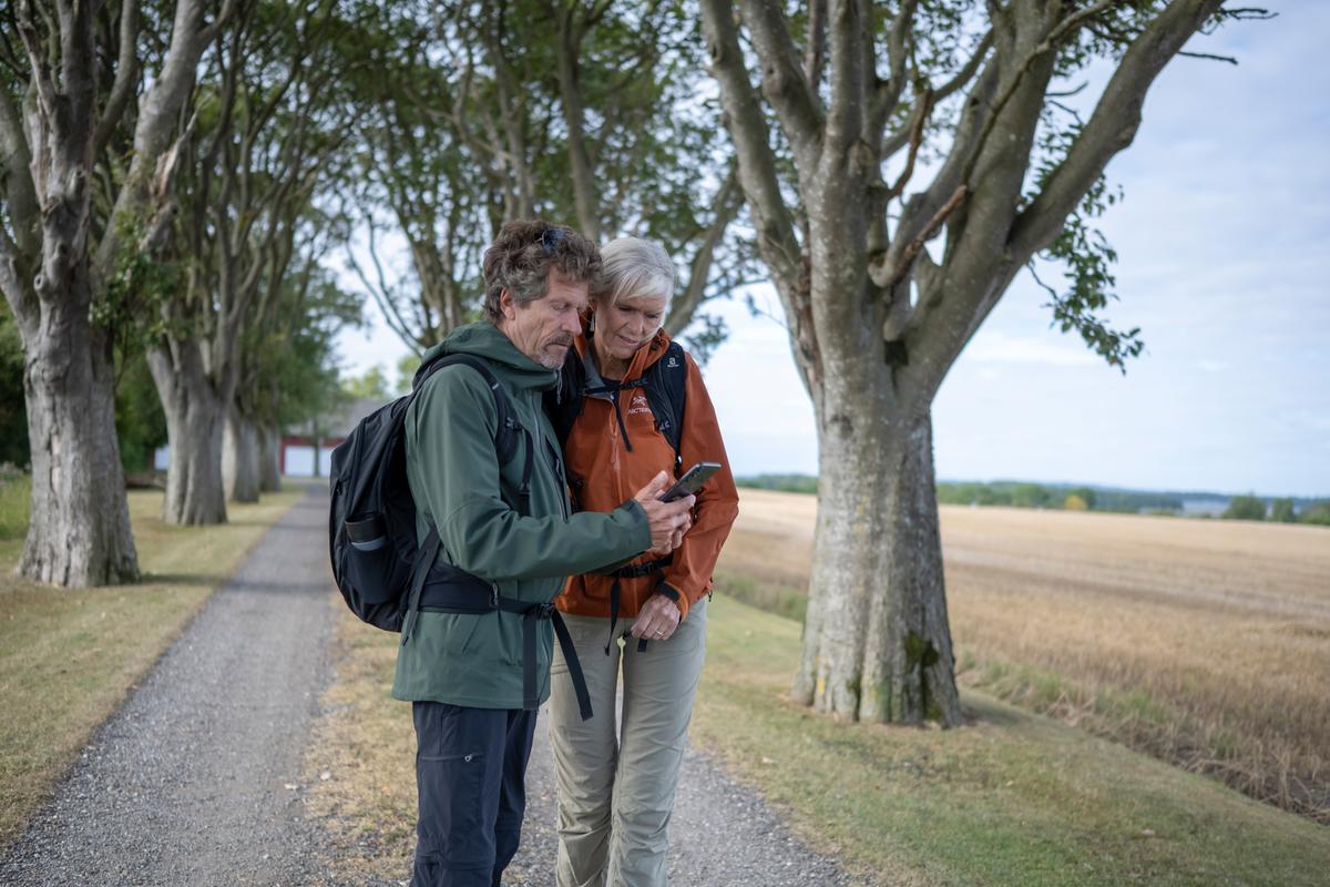 Mand og kvinde på vandretur står og kigger på VisitFyn-app'en på deres telefon