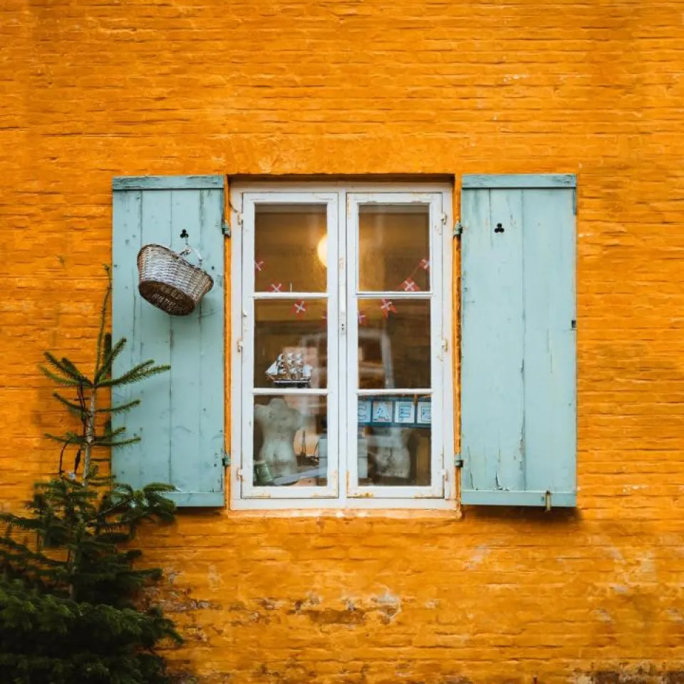 Vindue med lyseblå skodder på orange væg