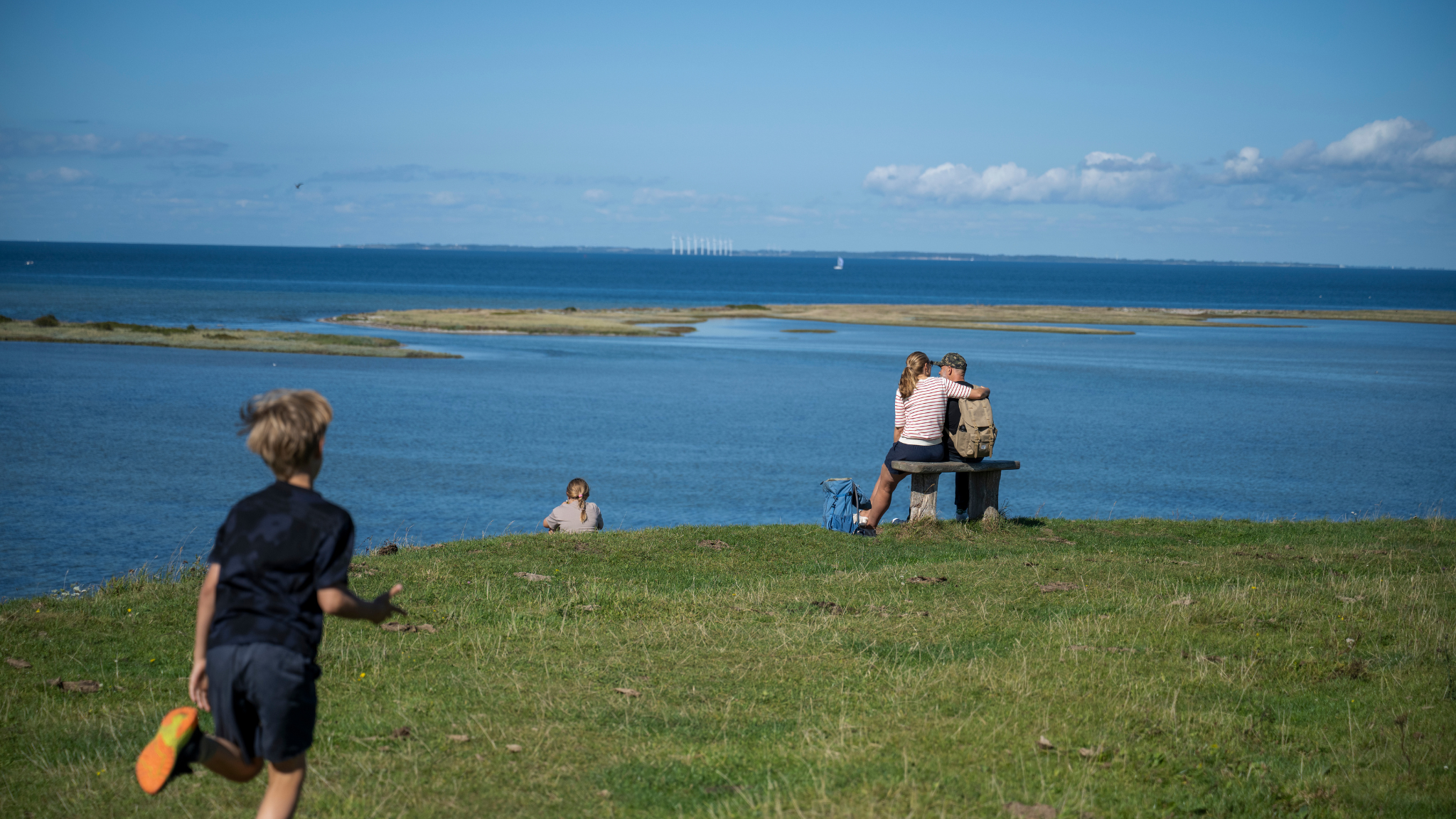 En familie nyder et udsigtspunkt på Fynshoved, hvor to forældre sidder på en bænk og børnene er i nærheden. 