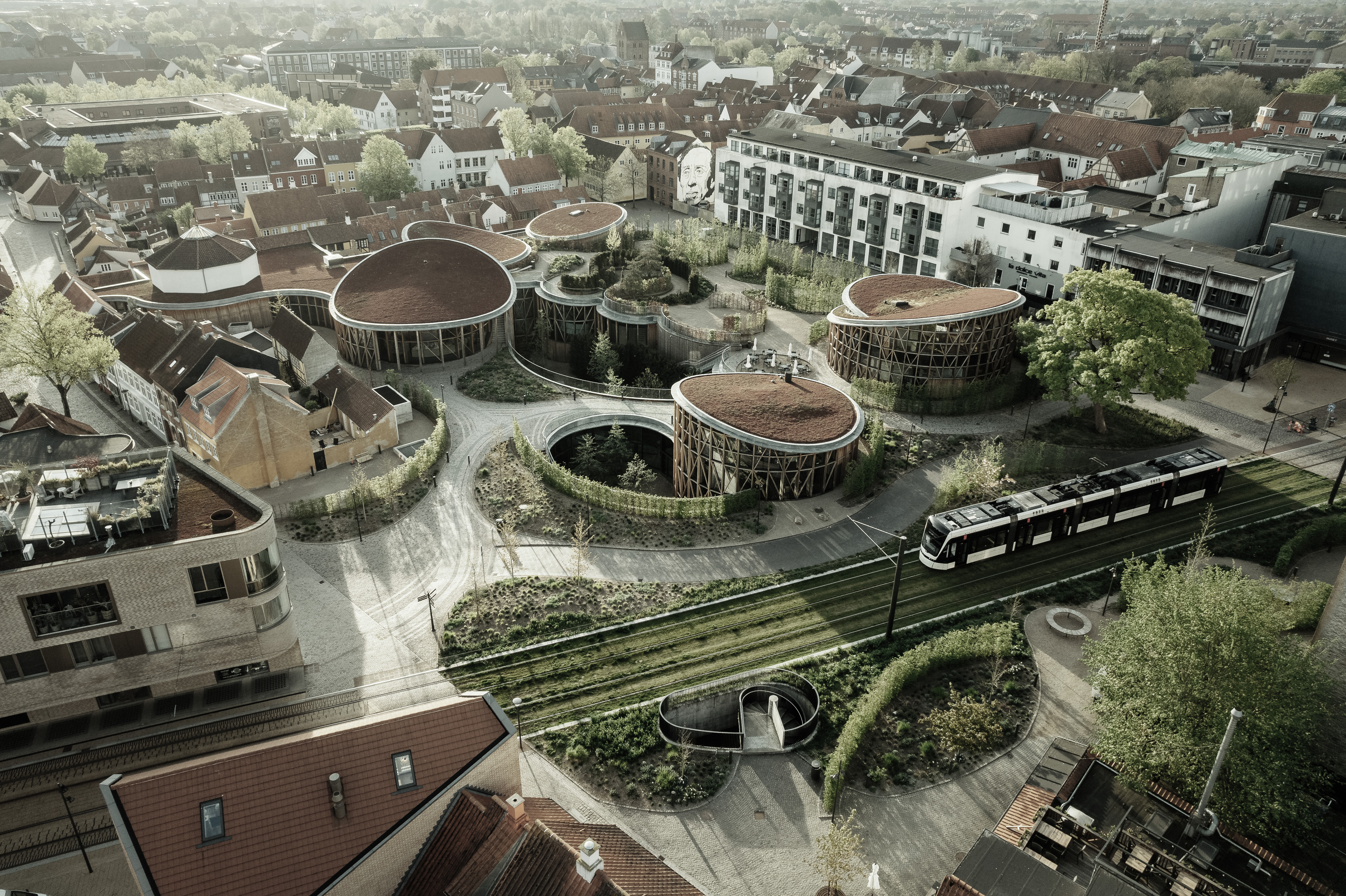 H.C Andersens Hus med de røde, runde, bølgende tage og letbanen i Odense set oppefra