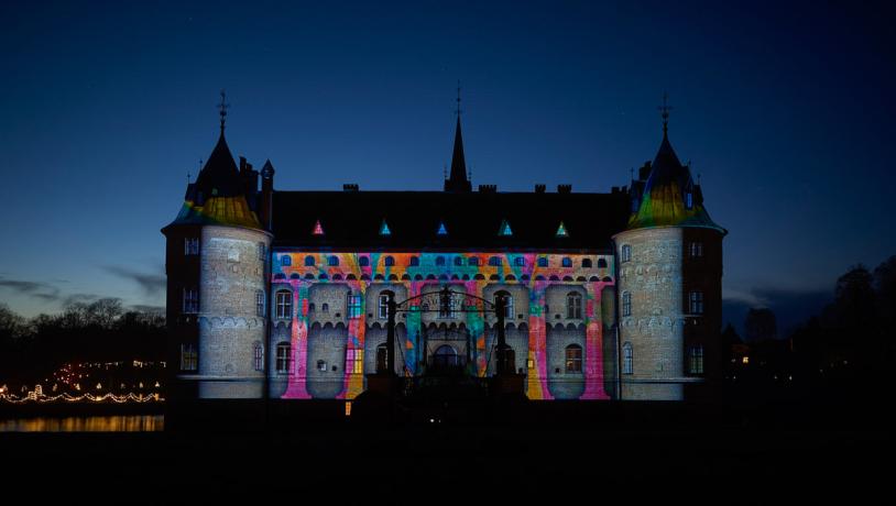 Egeskov slot ses i mørket. Facaden er lyst op i forskellig farvede mønstre.