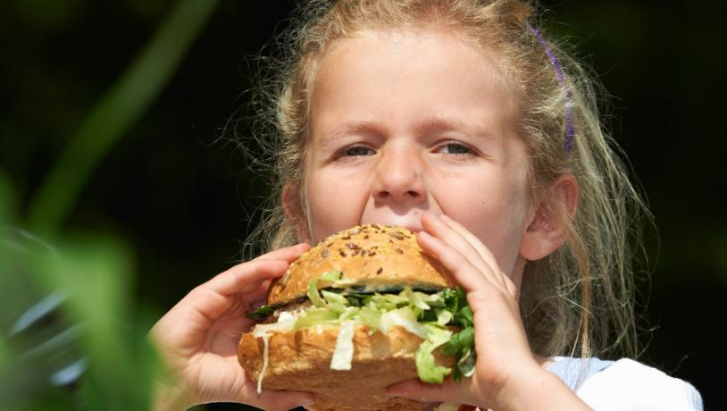En pige tager en stor mundfuld af en burger.