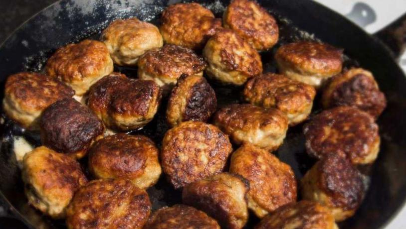 En stål stegepande fyldt med sydende frikadeller. 