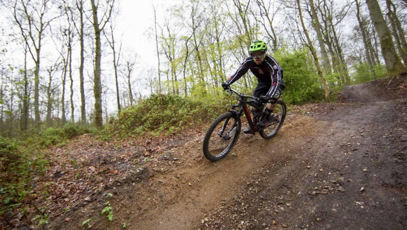 En mountainbiker med grøn hjelm cykler i skoven på vej ned ad en bakke.