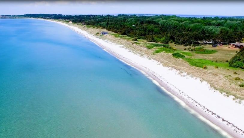 Luftfoto af en hvid sandstrand ud til tyrkisblåt vand 