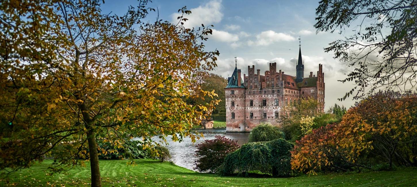 Egeskov Slot omgivet af træer og buske i efterårets farver.