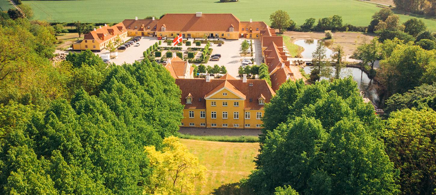 Et dronebillede af Broløkke Herregård med grønne marker og skov