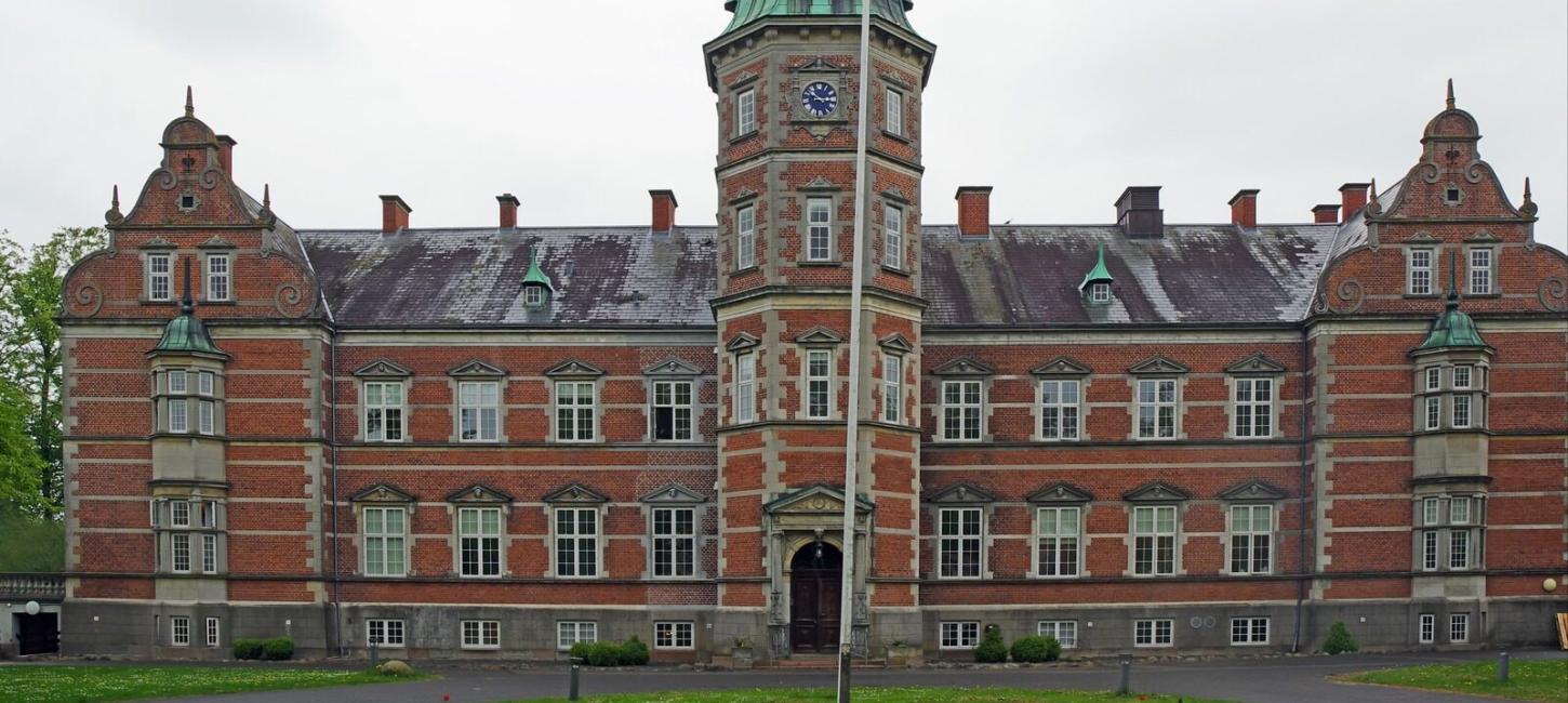 Flot rød herregård med sort tag og et stort tårn i midten.