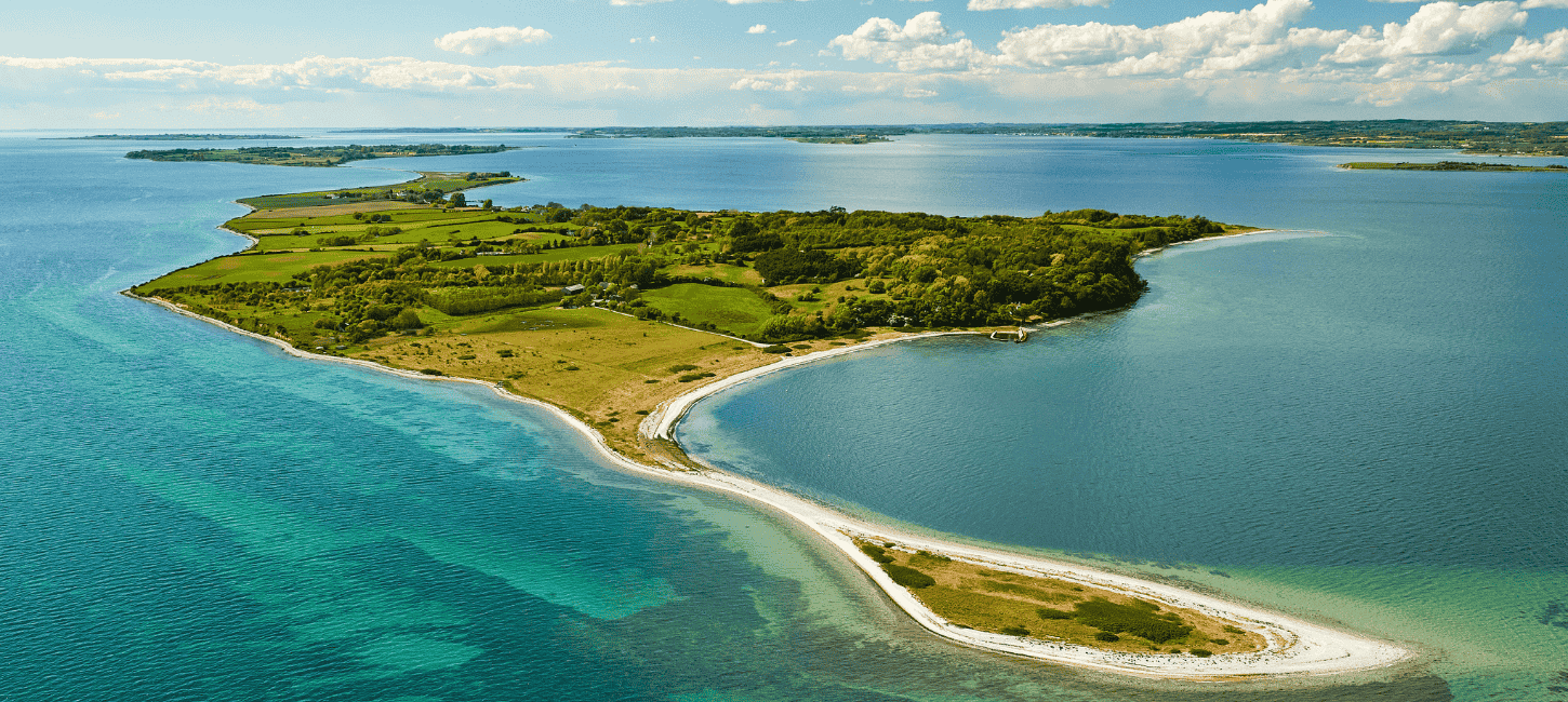 Drone photo of Avernakø in sharp, lush, green colors with oceanblue water all around the shores and the southfunen archipelago in the horizon