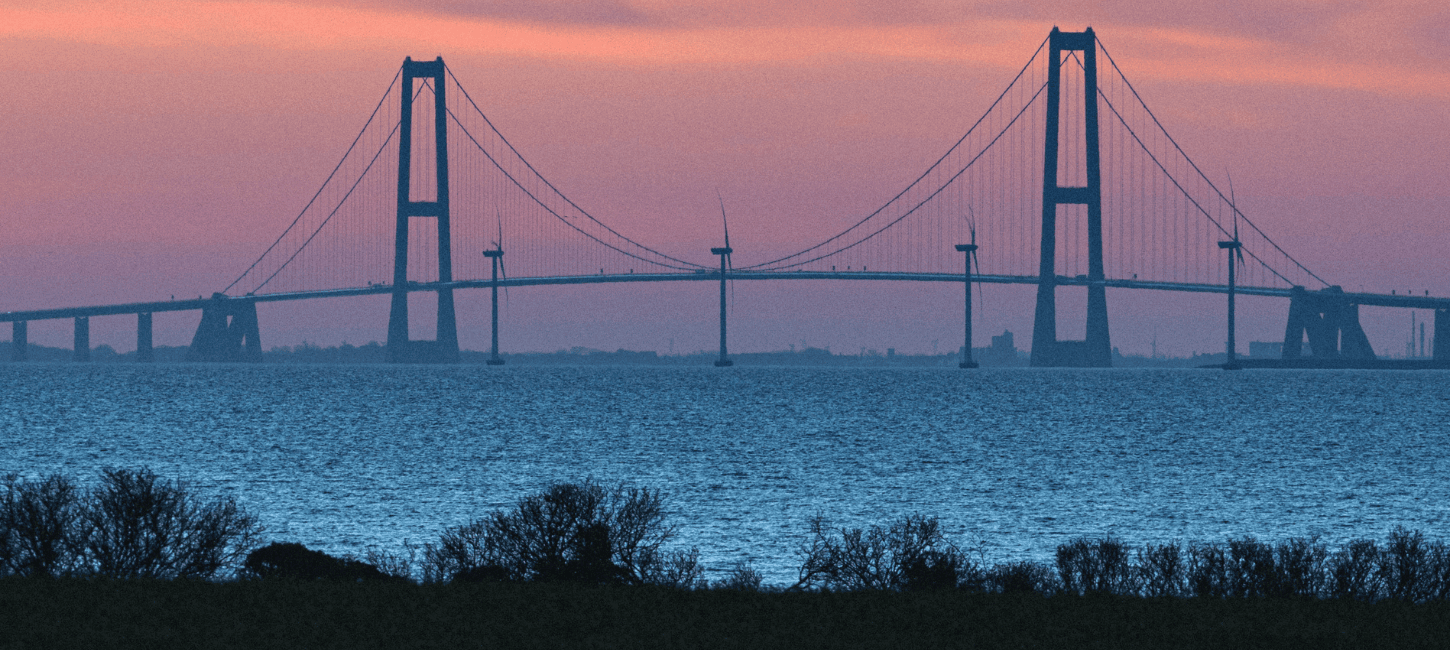 Storebæltsbroen i solnedgang, der forbinder Fyn og Sjælland over et stille vand.