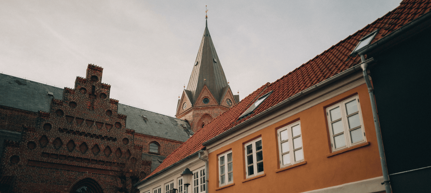 Et billede af tre forskellige bygningers tage og øverste dele, heriblandt et kirketårn