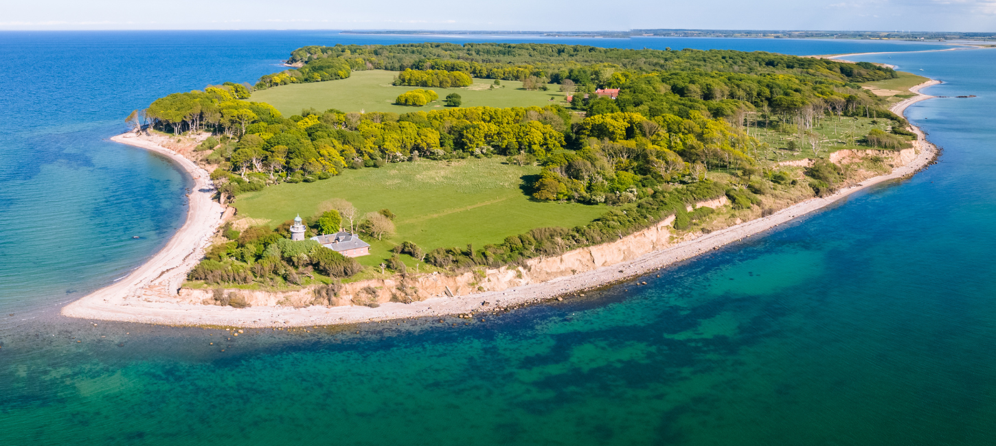 Dronefoto af en ø omringet af havet og som ikke er større end et par kvadratkilometer, med hvide kyster og grøn skov. 