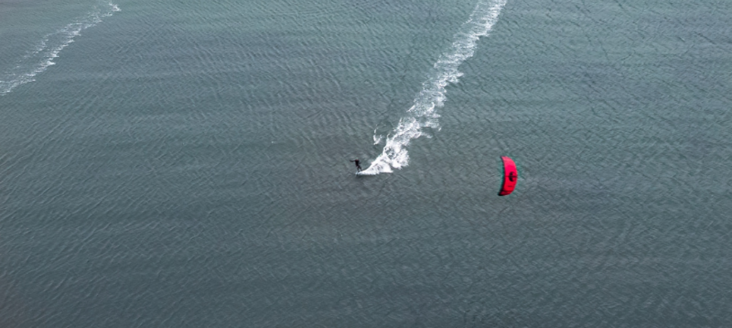 En kitesurfer med rødt sejl driver på stille vand ud for en dæmning