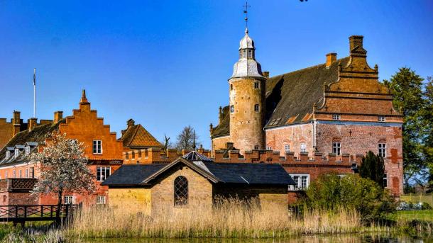 Prægtig slotsbygning i røde og gule mursten med tårn.