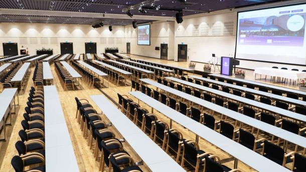 Et stort konferencelokale med stole, borde og tændte projektorer ved OCC Odense Congress Center. 