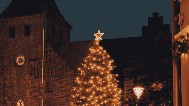 Højt juletræ med julebelysning og en kirke i baggrunden 