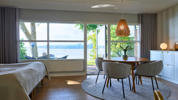 Et værelse set indefra med udsigt til Svendborg Sund, seng og borde og stole og naturfarvet indretning