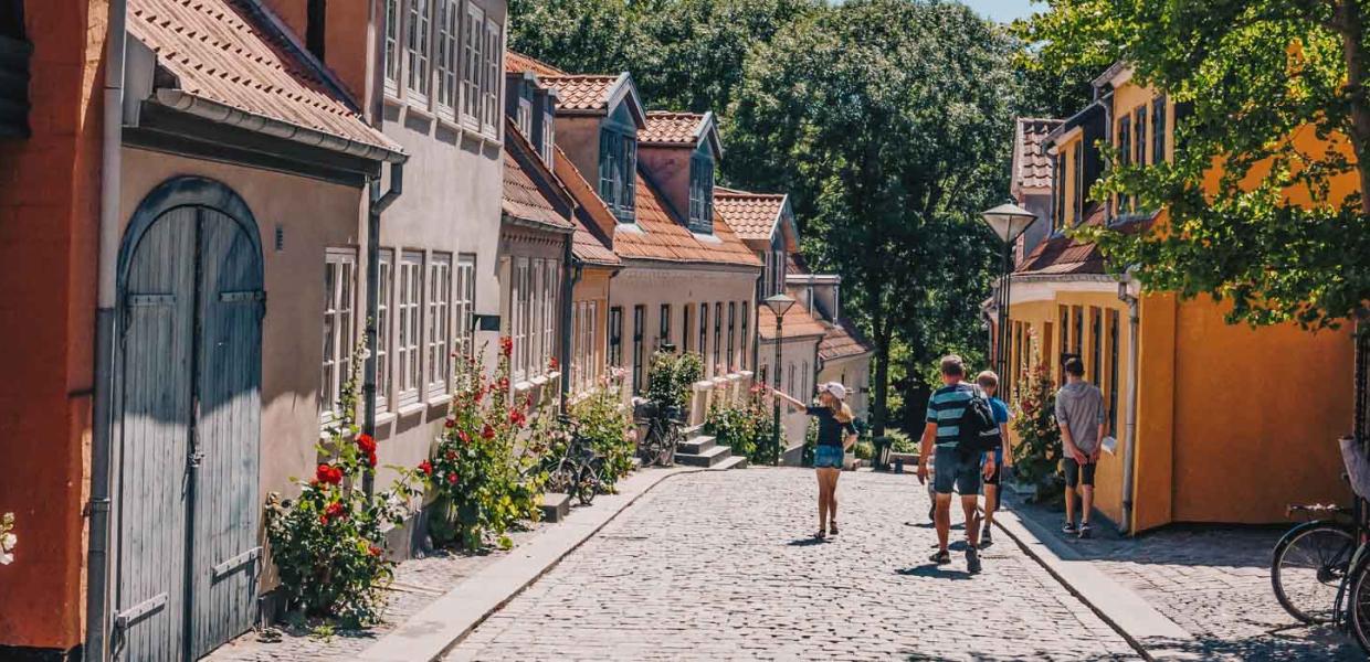 Fire personer i sommertøj ses gående ned ad Paaskestræde i Odense. Det er sommer og solen skinner.