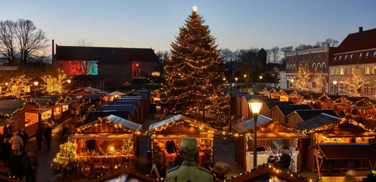 Hyggeligt julemarked set lidt oppefra med varme lys og et stort juletræ i midten.