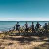 Fem cyklister står med deres cykler ved stranden og ser ud over havet. 