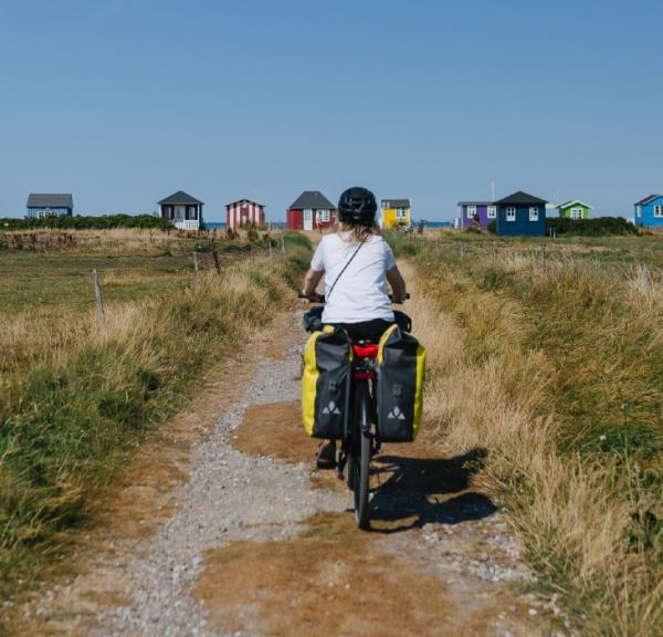 Kvindelig cyklist ses bagfra på vej ud til badehusene ved Vester Strand på Ærø. Det er sommer.