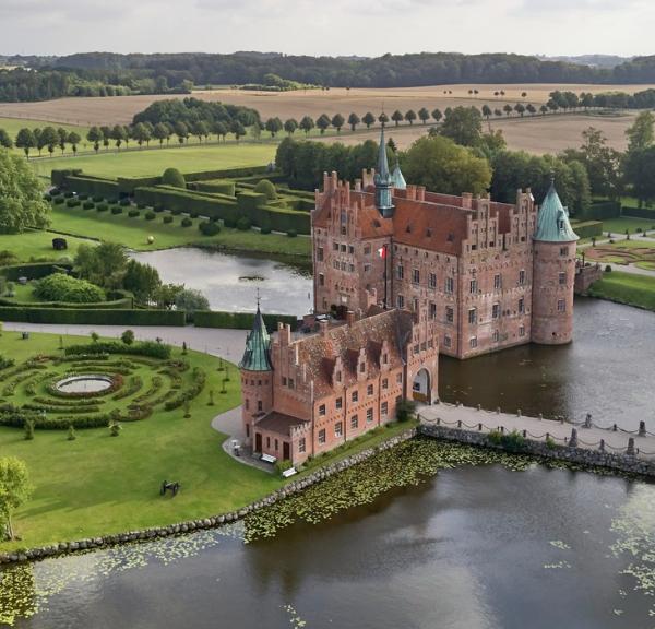 Egeskov Slot set oppefra med vand omkring og i grønne omgivelser.