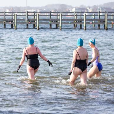 Tre vinterbadere med handsker og hætter på vej ud i vandet.