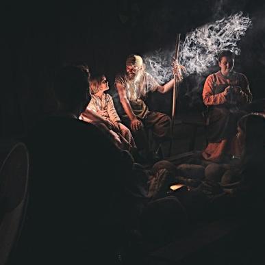 Et dunkelt rum oplyses af en enkelt solstråle, der oplyser en lille flok vikingeklædte mennesker 
