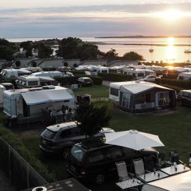 Solnedgang over havet og en fyldt campingplads.