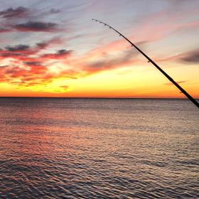 Den smukkeste gul-orange solnedgang ud over havet. I forgrunden til højre i billedet ses en fiskestang.