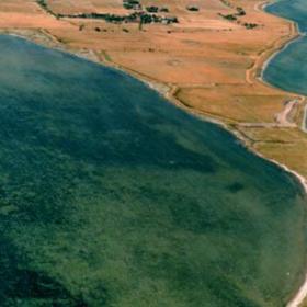 Dronefoto af den smalle tange ud til Birkholm, omgivet af vand til begge sider.