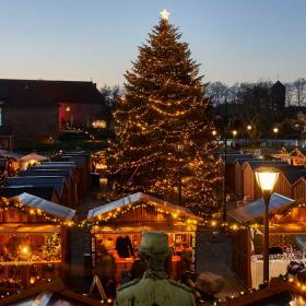 Hyggeligt julemarked set lidt oppefra med varme lys og et stort juletræ i midten.