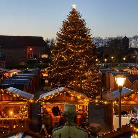 Hyggeligt julemarked set lidt oppefra med varme lys og et stort juletræ i midten.