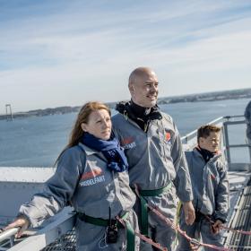 Fire mennesker på et gråt stillads. De er på bridgewalking på den gamle Lillebæltsbro. I baggrunden anes den nye Lillebæltsbro.