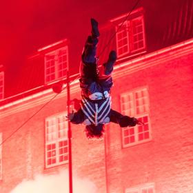 Odenses rådhus er lyst op i rød. Foran bygningen er en mand i cirkus tøj på vej rundt i en baglæns salto.