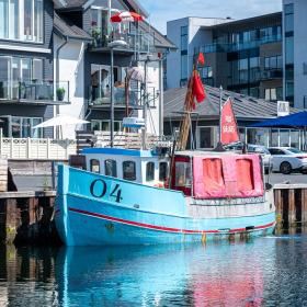 Havn med lyseblå båd i forgrunden og hvide bygninger i baggrunden.