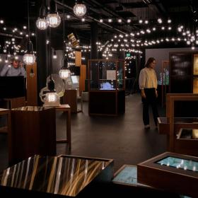 En kvinde og en mand udforsker en udstilling. Lokalet er mørkt med udstillingsmontrer og en masse lamper med lysende pærer i loftet.