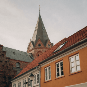 Et billede af tre forskellige bygningers tage og øverste dele, heriblandt et kirketårn