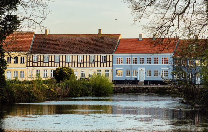 Nogle farverige bindingsværkfacader ligger i baggrunden af en stille sø på en forårsdag